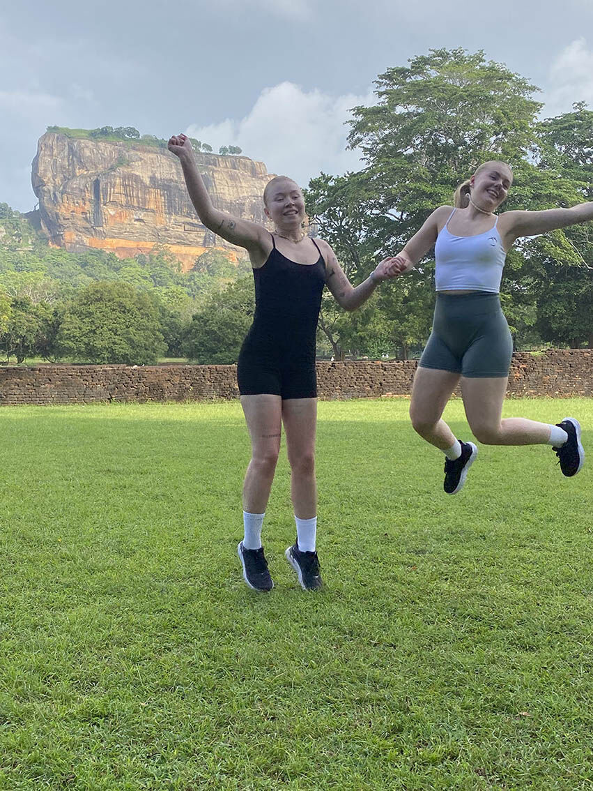 Two travellers jumping on the lawn below Sigiriya rock