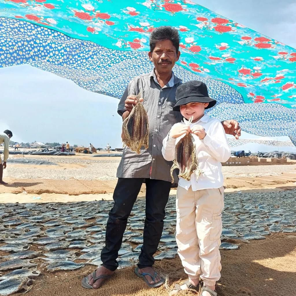 A fisherman and a child holding dried fish on the beach